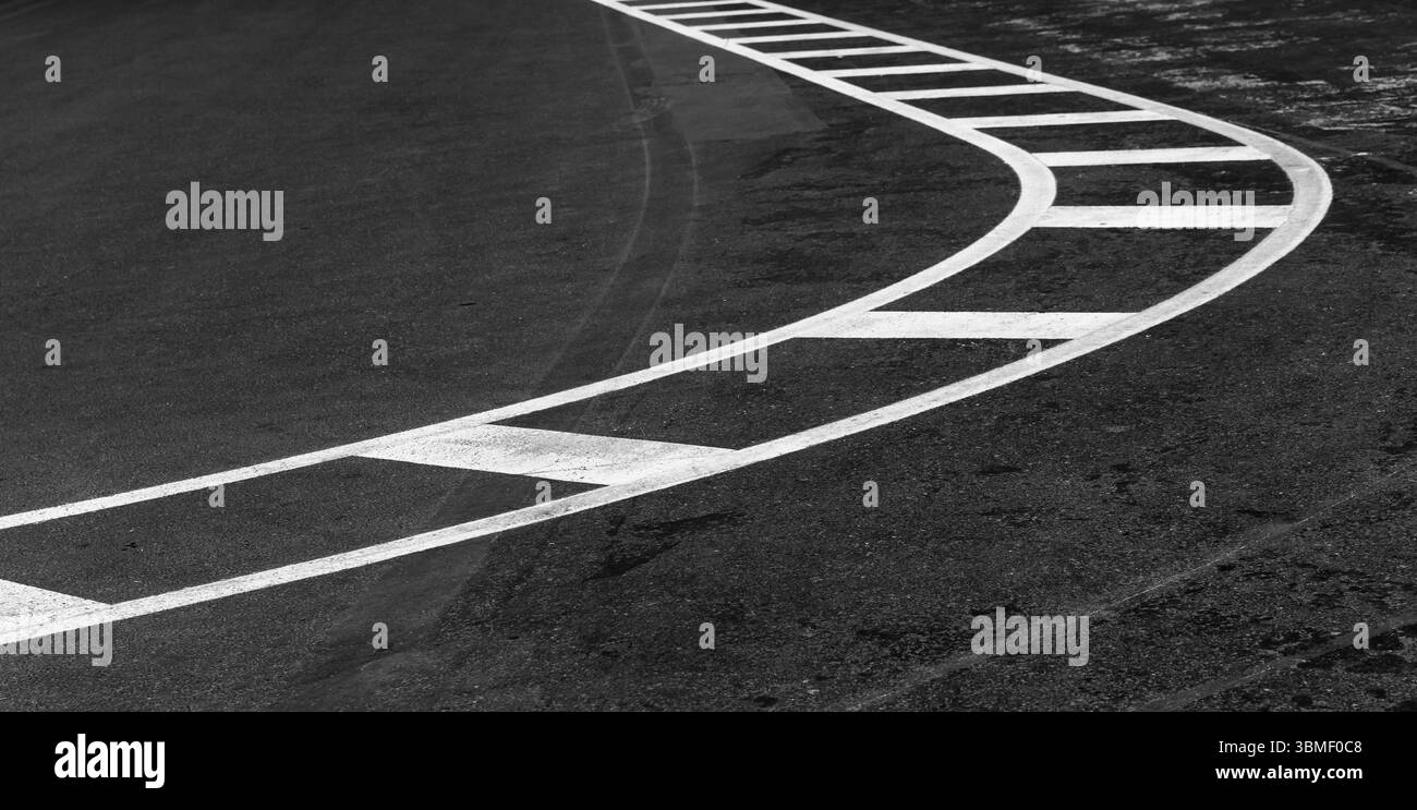 Una rappresentazione monocromatica di una strada asfaltata curva adornata da linee di demarcazione della corsia bianche dinamiche, che enfatizzano il movimento, la guida e la struttura urbana Foto Stock