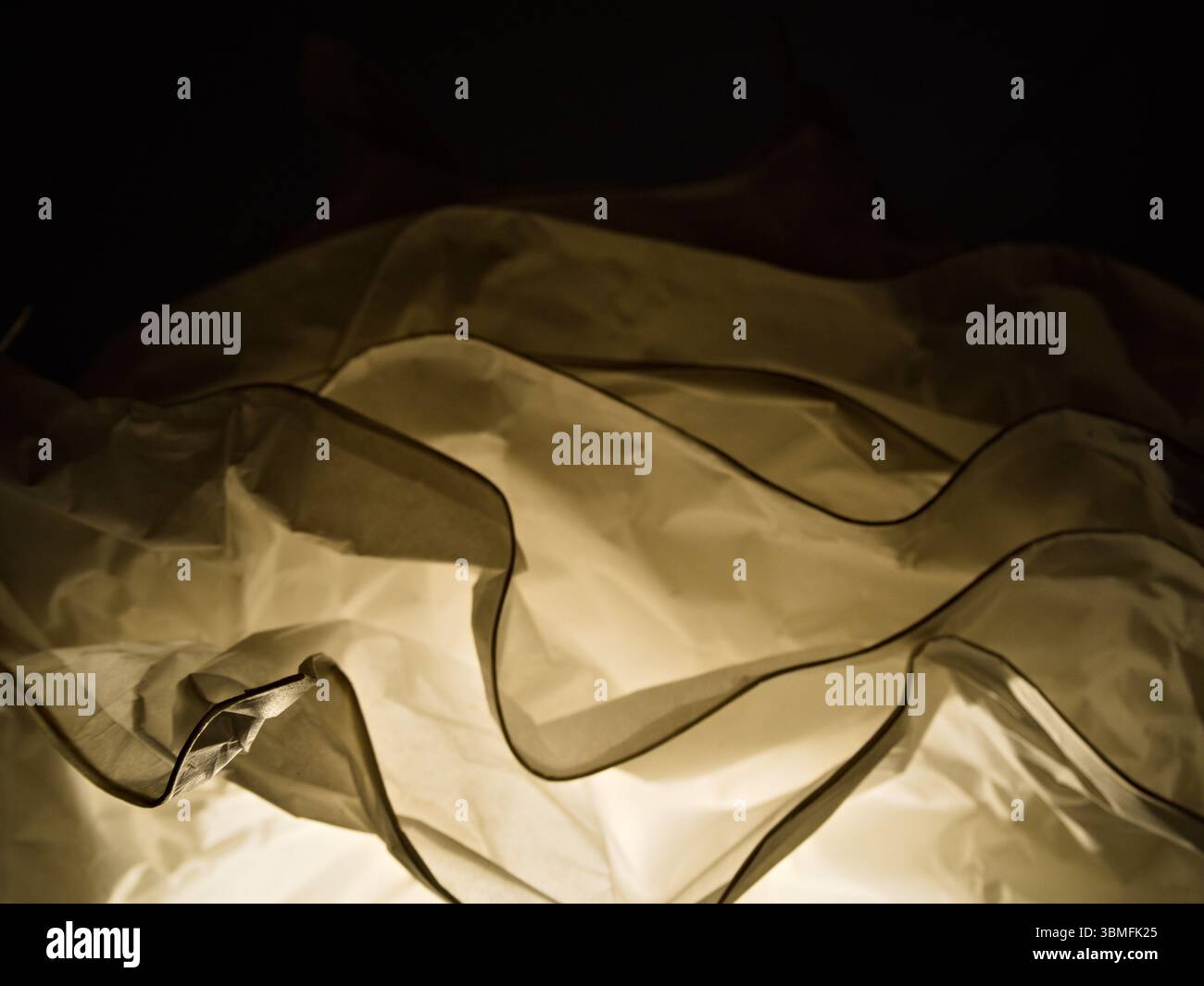 La luce calda illumina la struttura astratta a strati della carta, proiettando ombre e creando profondità su uno sfondo scuro. Foto Stock