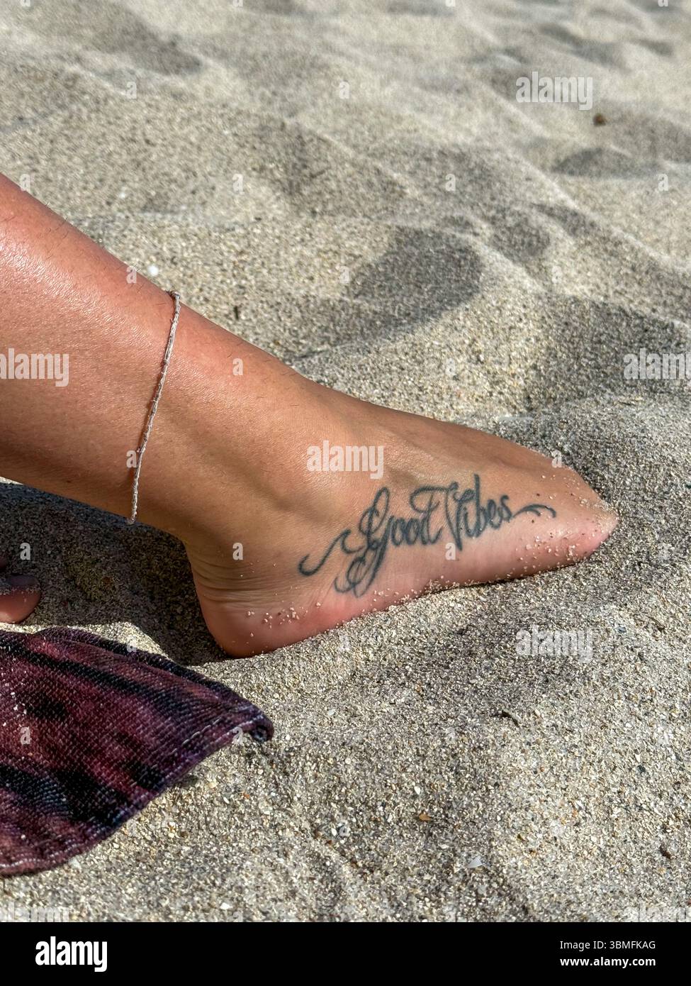 Giovane donna su telo da spiaggia con piede tatuato in sabbia bianca Foto Stock
