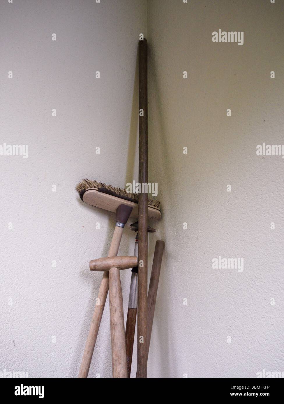 Primo piano di un mucchio di attrezzi rustici in legno collocati nell'angolo della facciata di un edificio, con maniglie in legno visibili e la parte superiore di una scopa. Foto Stock