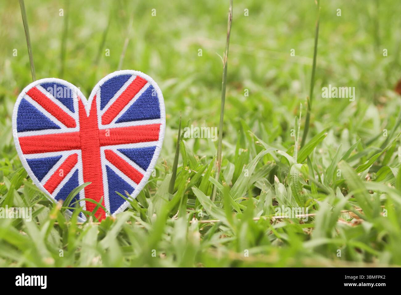 Union Jack ricamato a forma di cuore su erba verde, design ecocompatibile con spazio copia, simbolo di amore e sostenibilità. Foto Stock