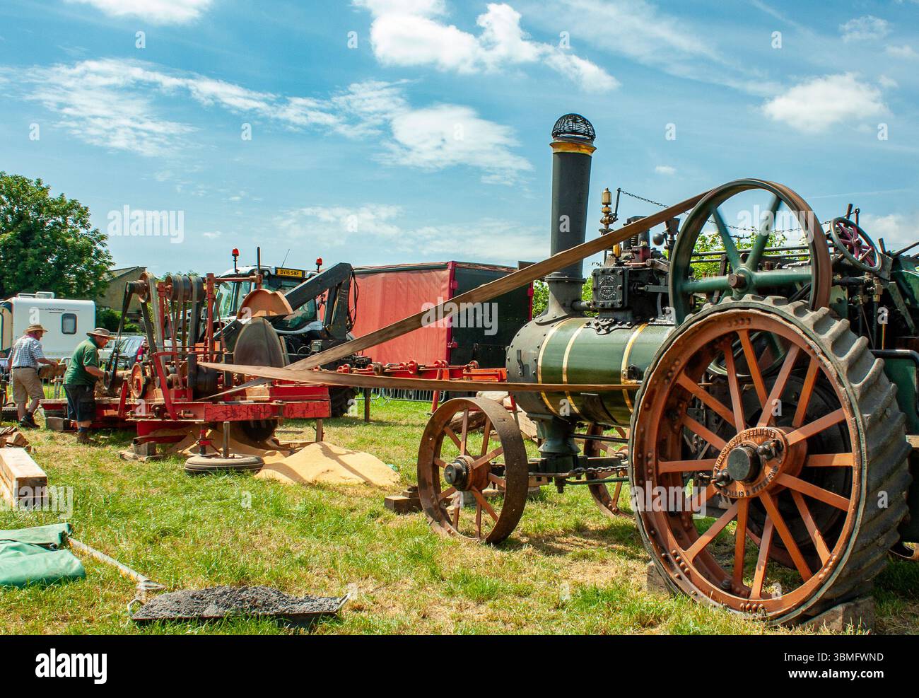 Un vecchio motore a vapore che alimenta macchinari con cinghie in occasione di un evento agricolo all'aperto in una giornata di sole Foto Stock