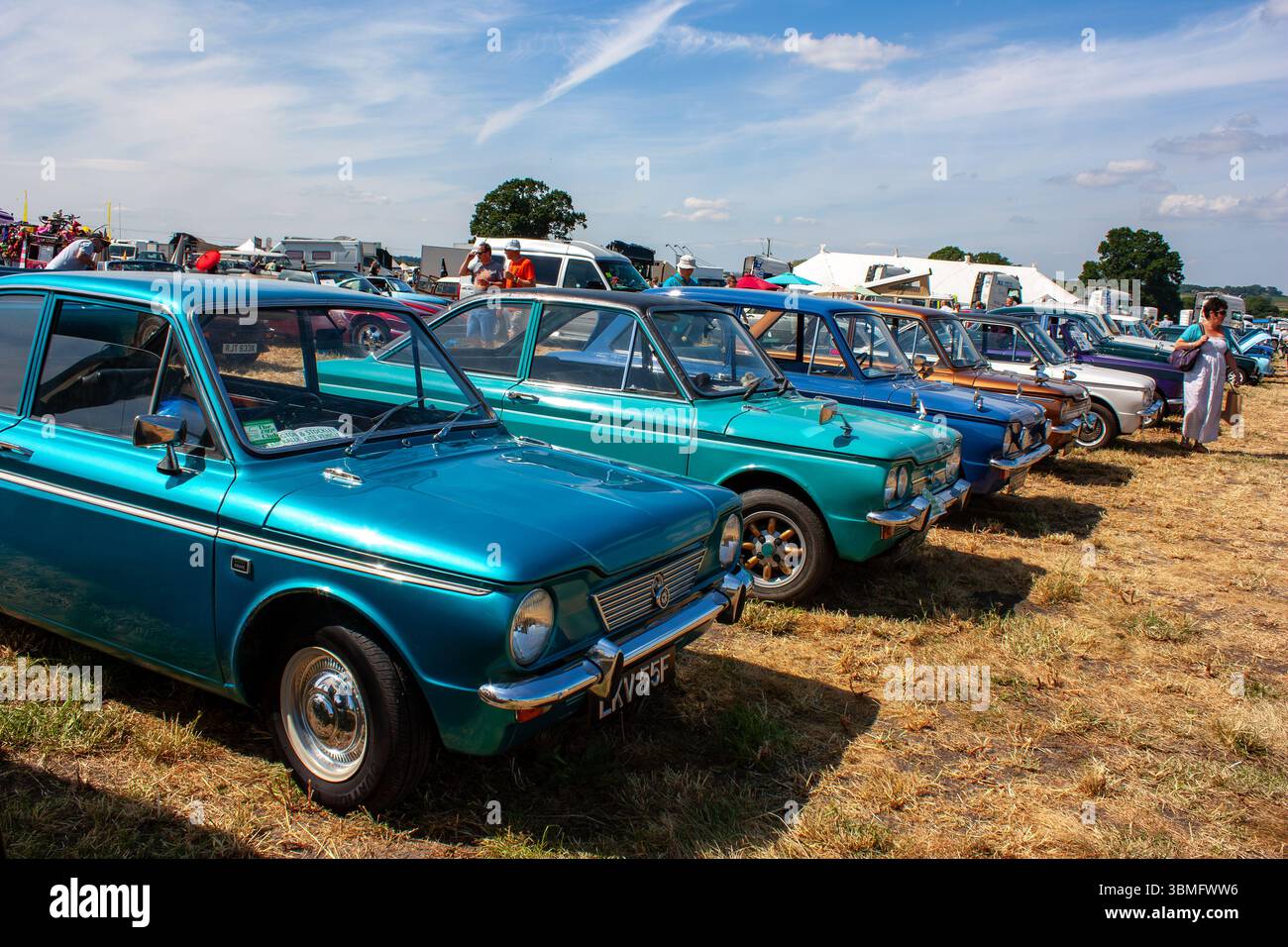 Linea di camoscio blu d'epoca Singer parcheggiate all'aperto in occasione di un evento di auto d'epoca in una giornata di sole con persone sullo sfondo Foto Stock