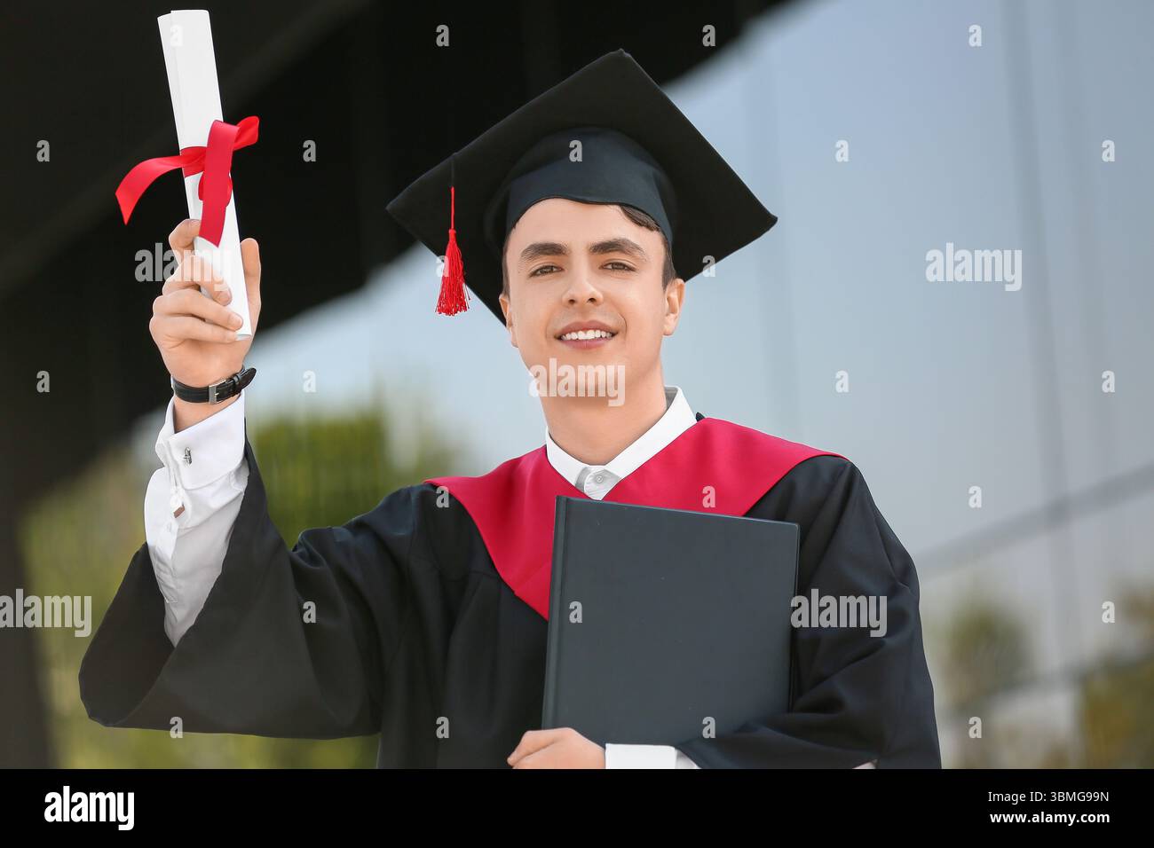 Studente laureato con diploma e libro vicino all'università Foto Stock