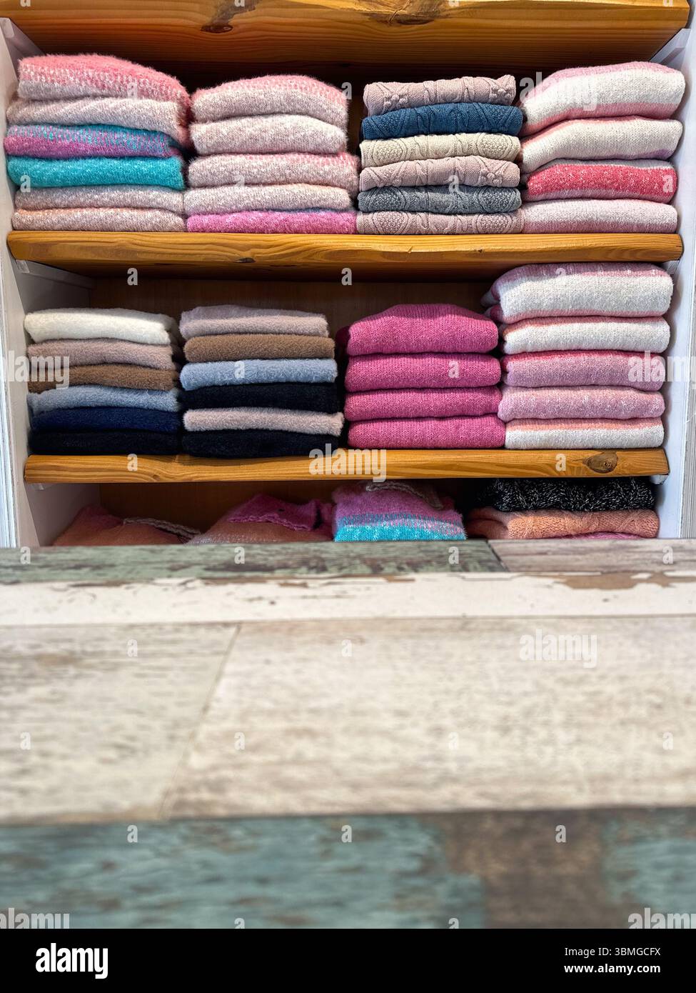 Tavolo in legno bianco sporco con finitura patina in primo piano. Sullo sfondo delicatamente focalizzato, i capi sono ben piegati in tinte pastello Foto Stock