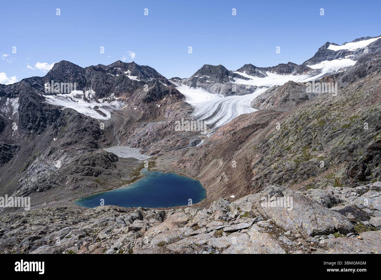 Lago glaciale blu in un paesaggio roccioso di montagna, dietro il Koenigshofspitz e il ghiacciaio Uebeltalferner, discesa dalla cima del Roter Grat, Alpi dello Stubai Foto Stock
