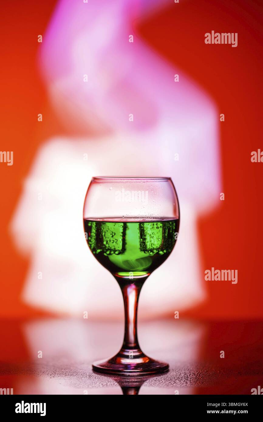 Un bicchiere con un drink su uno splendido sfondo rosso illuminato con luce colorata Foto Stock