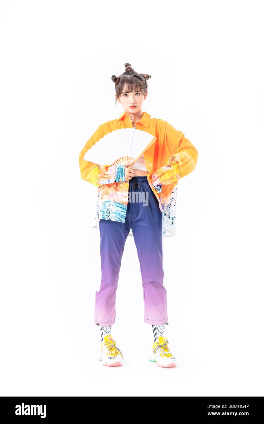 Una giovane donna alla moda in una giacca di ispirazione cinese tradizionale gioca con un ventilatore cinese pieghevole in carta, senza sforzo cool​ Foto Stock