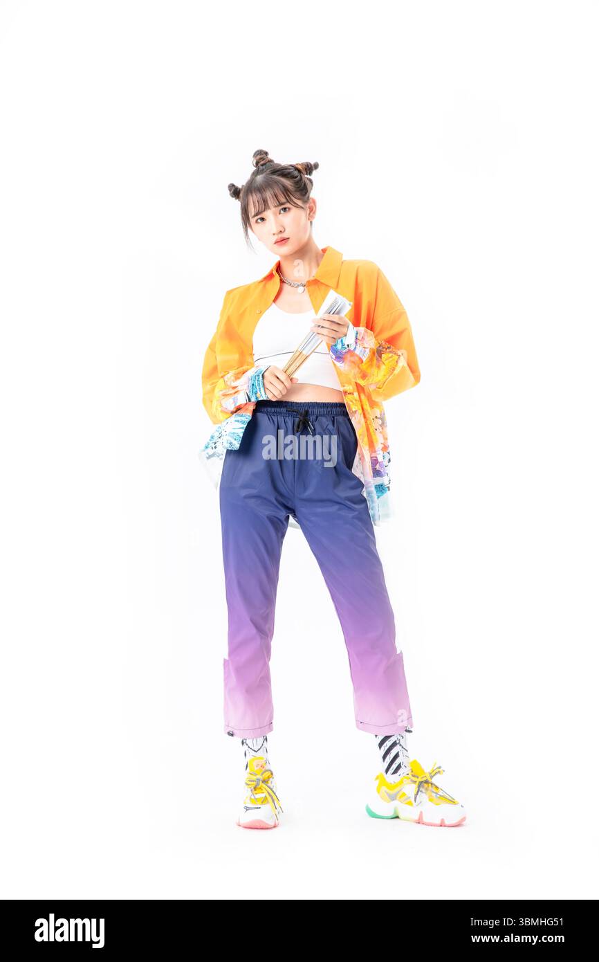 Una giovane donna alla moda in una giacca di ispirazione cinese tradizionale gioca con un ventilatore cinese pieghevole in carta, senza sforzo cool​ Foto Stock