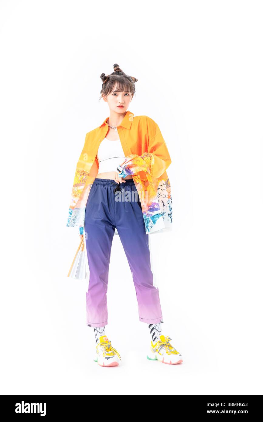 Una giovane donna alla moda in una giacca di ispirazione cinese tradizionale gioca con un ventilatore cinese pieghevole in carta, senza sforzo cool​ Foto Stock