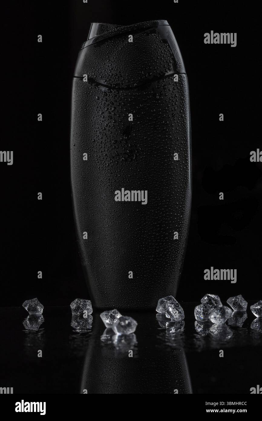 Flacone in plastica nera sudata per shampoo o gel doccia su sfondo nero isolato. ci sono anche cubetti di ghiaccio sullo sfondo Foto Stock