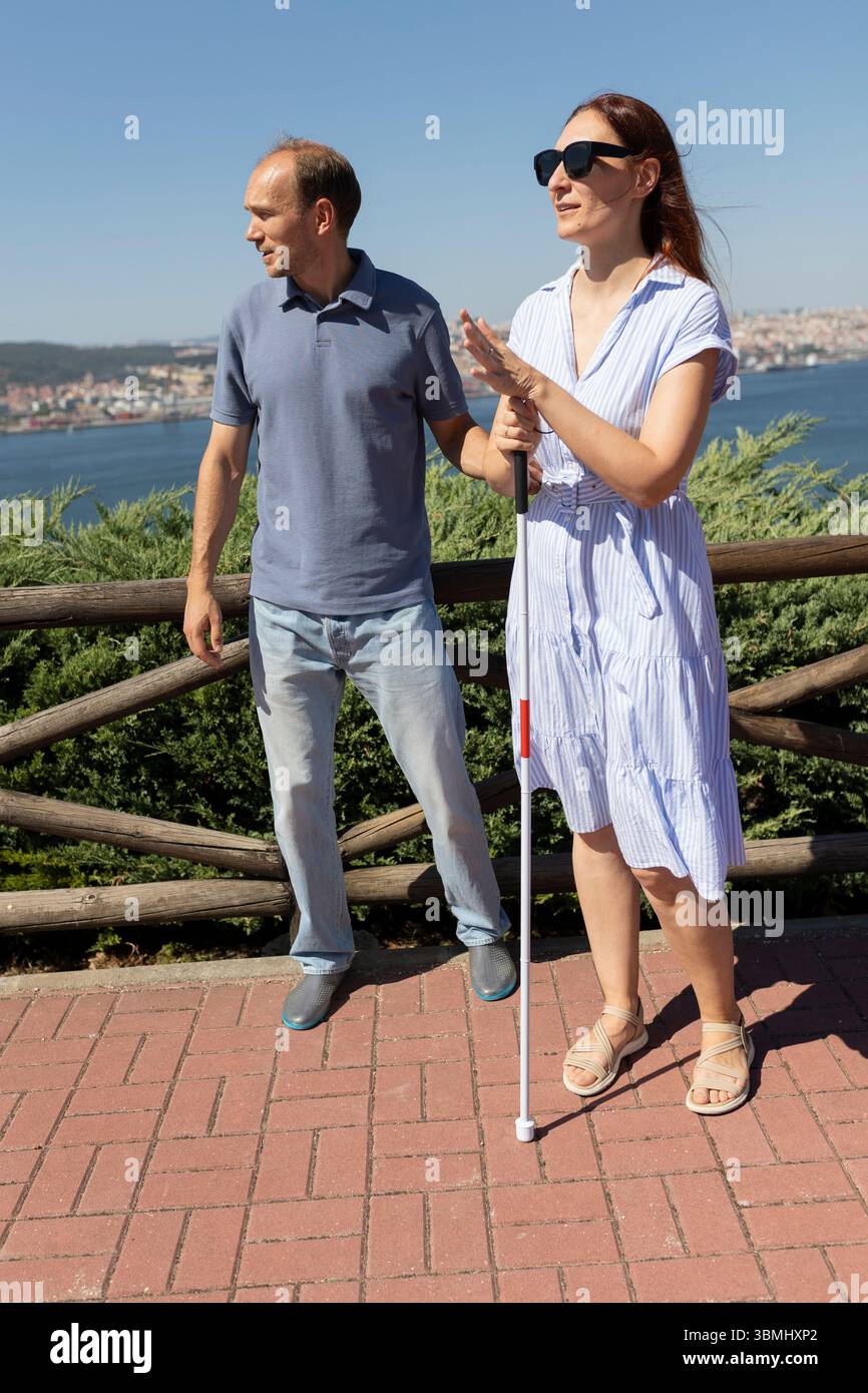 Donna cieca che tiene il bastone bianco che parla con un uomo all'aperto Foto Stock
