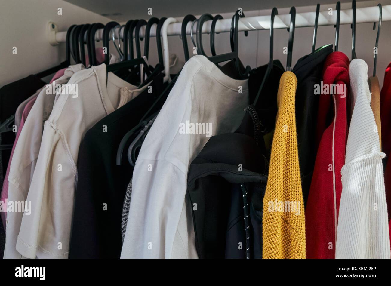 Armadio pieno di vestiti, tra cui una camicia bianca e un maglione rosso. La camicia bianca è sul lato sinistro dell'armadio, mentre il maglione rosso è sul Foto Stock