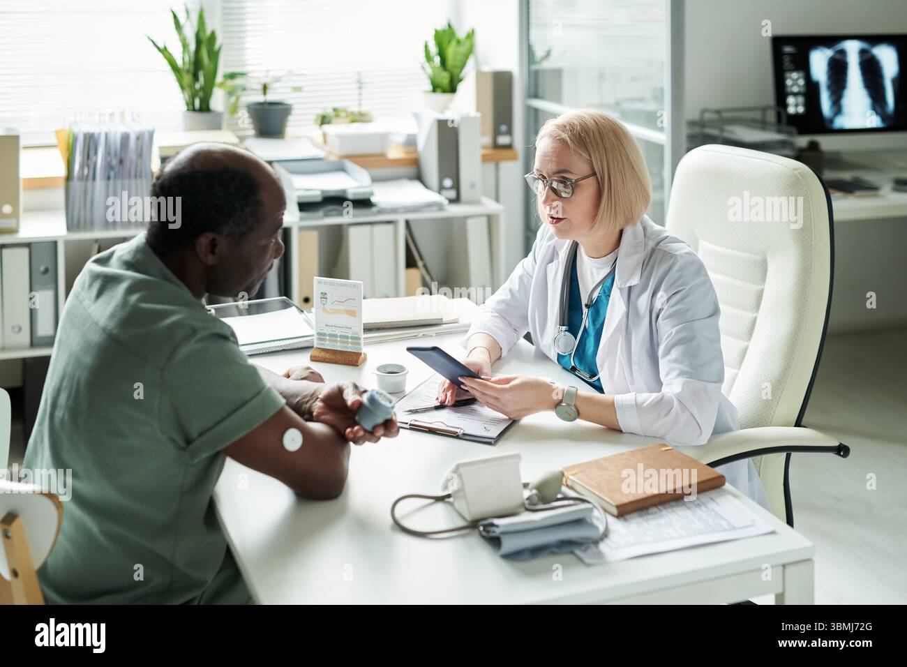 Uomo nero di mezza età seduto di fronte al medico donna caucasico discutere di gestione del diabete durante la consultazione medica in ufficio moderno, sangue g Foto Stock