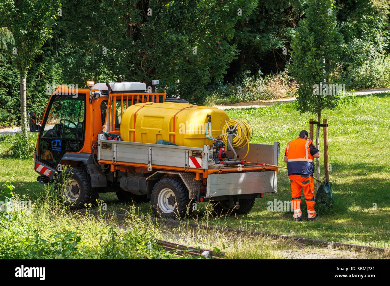 Un dipendente dei servizi comunali riempie una sacca di irrigazione su un giovane albero in un parco di Wetter an der Ruhr, Renania settentrionale-Vestfalia, Germania e in Mitarb Foto Stock