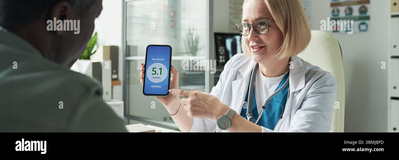Medico caucasico di mezza età che mostra la lettura digitale del glucosio su smartphone fino a paziente di mezza età di uomo nero durante la consultazione per il diabete in medicina Foto Stock