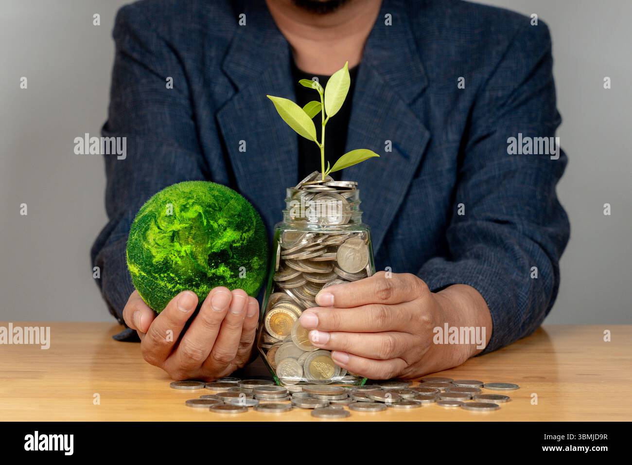 Primo piano di monete da uomo che salvano le mani in vaso accanto al globo verde, simboleggiando abitudini finanziarie eco-consapevoli. Foto Stock