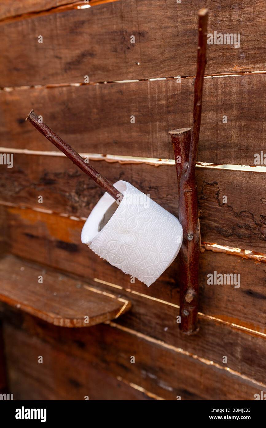 Rotolo di carta igienica appeso su un supporto realizzato a mano con rami di alberi naturali, fissato a una parete di legno in un ambiente rustico ed ecologico del bagno Foto Stock