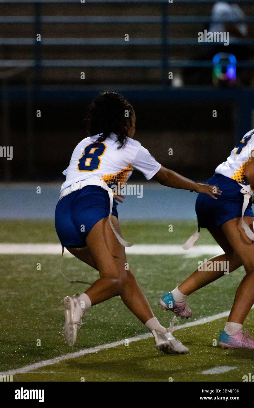 Una giocatrice di flag football si carica in avanti con determinazione durante una partita notturna. Cattura velocità, messa a fuoco e spirito competitivo con le luci da stadio Foto Stock