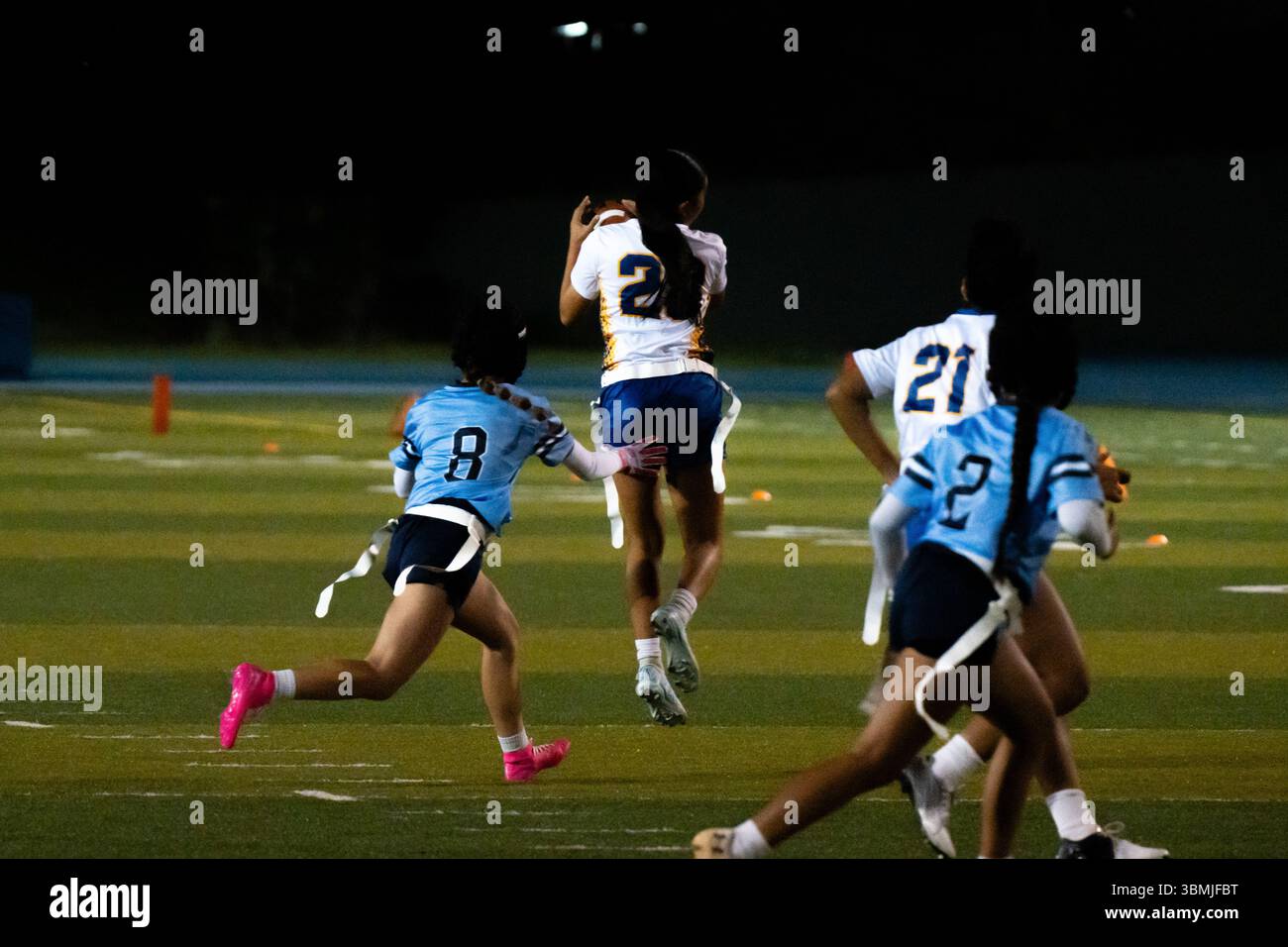 Le ragazze sbandierano l'azione calcistica durante la partita notturna, le giocatrici saltano per catturare la palla a mezz'aria mentre i difensori inseguono, energico momento sportivo scolastico, atletica giovanile Foto Stock