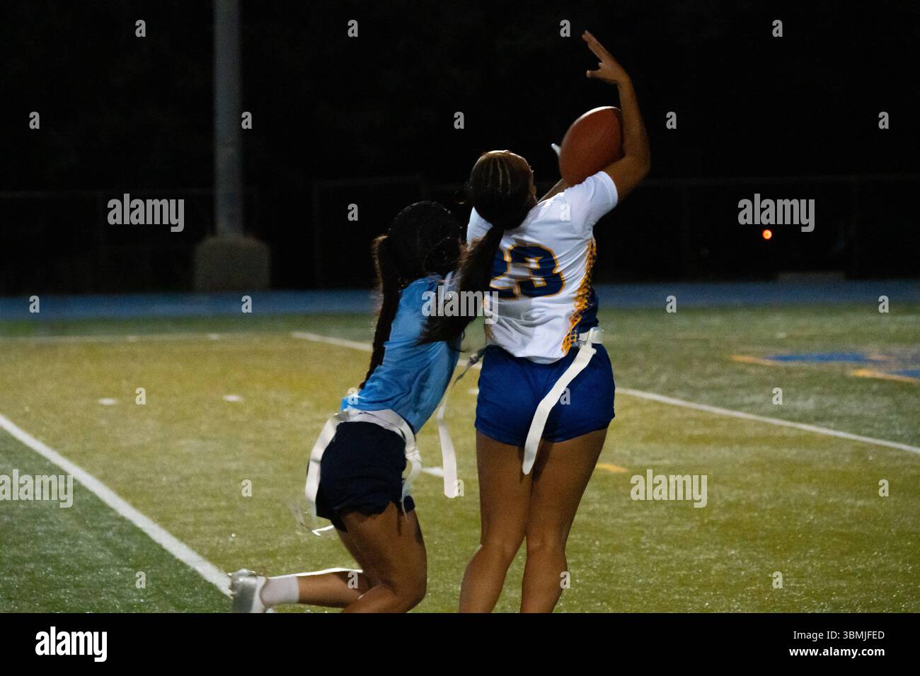 Le ragazze sbandierano l'azione calcistica durante la partita notturna, le giocatrici saltano per catturare la palla a mezz'aria mentre i difensori inseguono, energico momento sportivo scolastico, atletica giovanile Foto Stock