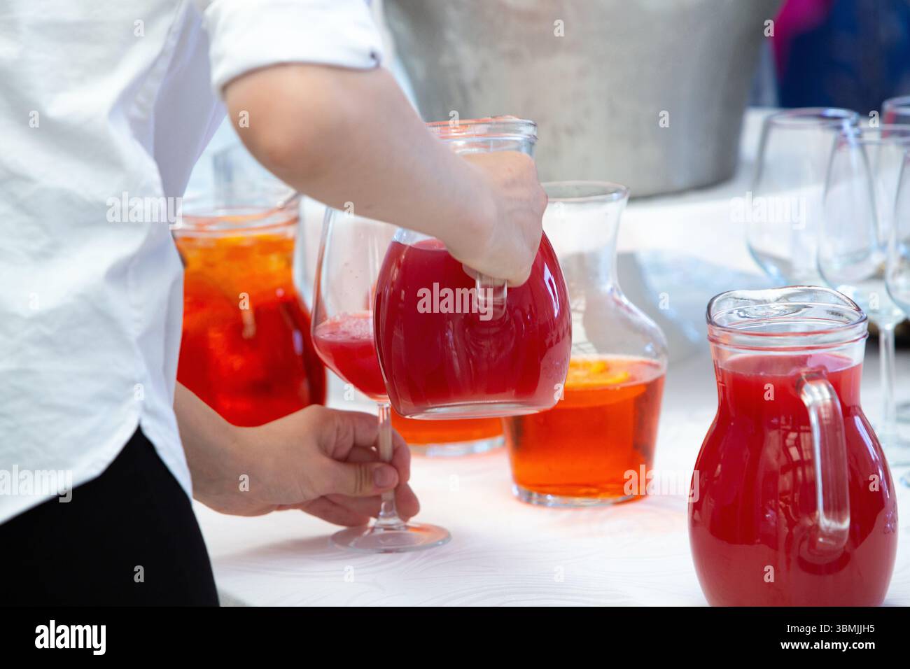 Servizio catering per preparare bevande per gli ospiti, versare succo di frutta rosso in un bicchiere durante un evento all'aperto Foto Stock