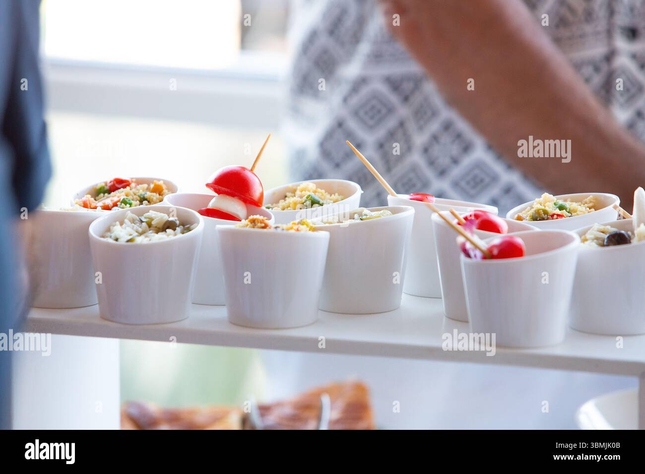 Piccole ciotole bianche piene di vari antipasti, tra cui riso, verdure e pomodori ciliegini, pronte per essere servite in occasione di un evento con servizio catering Foto Stock