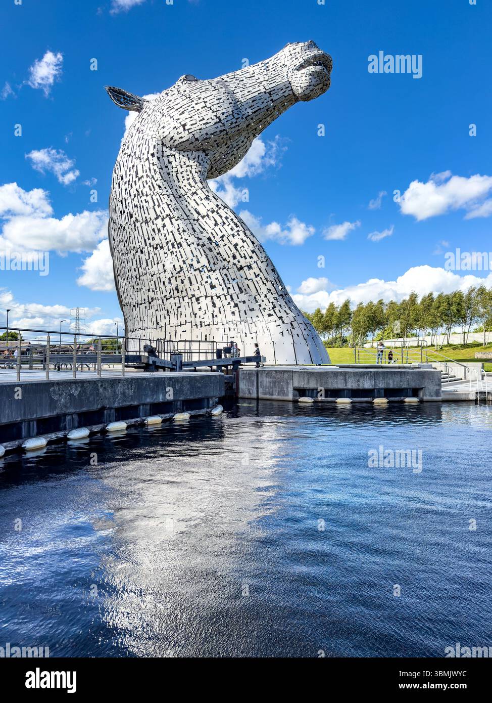 Maestosa grande scultura a testa di cavallo conosciuta come Kelpies, che si riflette nell'acqua sotto un cielo nuvoloso blu in un parco di Falkirk, scozia Foto Stock
