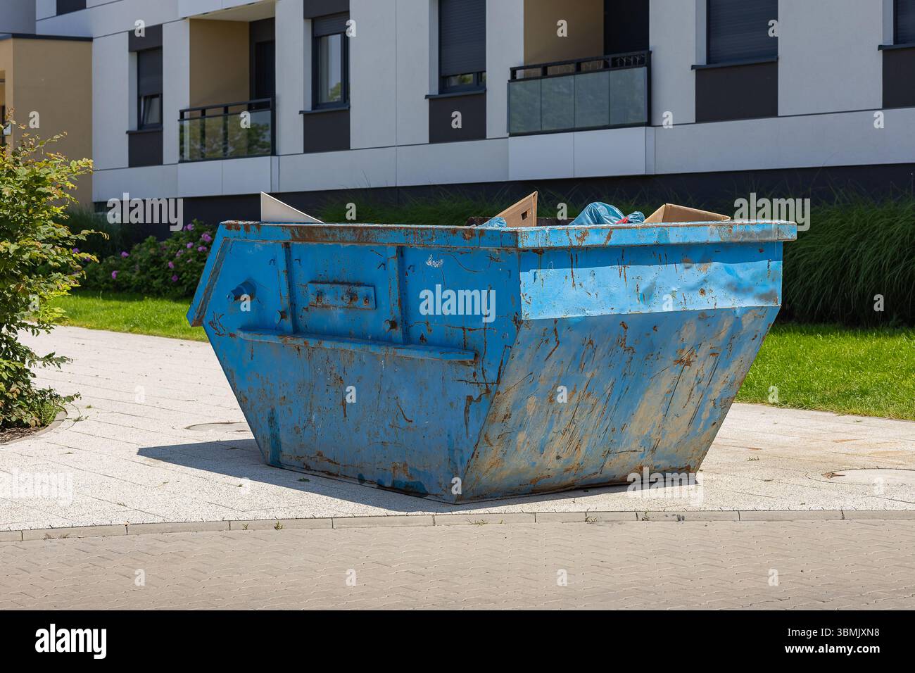 Grande contenitore con cassonetti blu arrugginito situato vicino al moderno edificio di appartamenti. Gestione dei rifiuti residenziali, pulizia e organizzazione di proprietà all'aperto Foto Stock