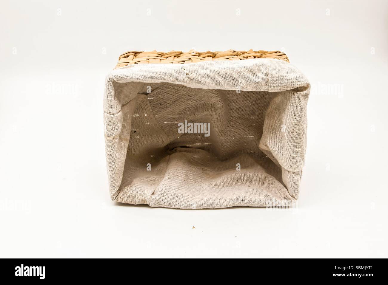 Cestello in vimini con rivestimento in lino beige mostrato lateralmente, vuoto, per riporre la casa e organizzare il tutto su sfondo bianco. Foto Stock