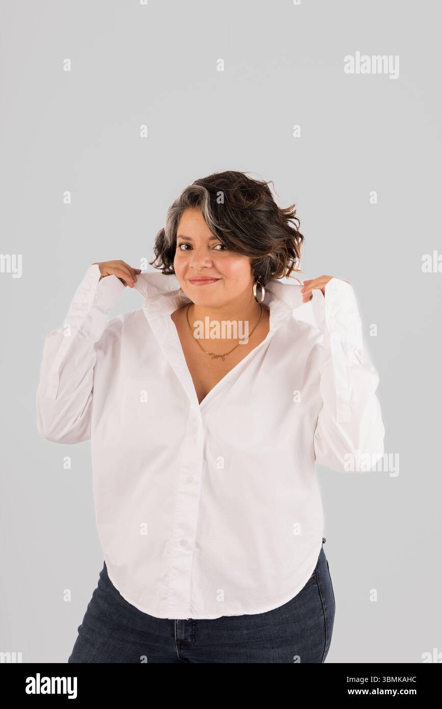 Una donna con una camicia bianca sta posando per una foto. Indossa una collana e i capelli vengono tirati indietro. Concetto di fiducia e di autoassicurazione Foto Stock