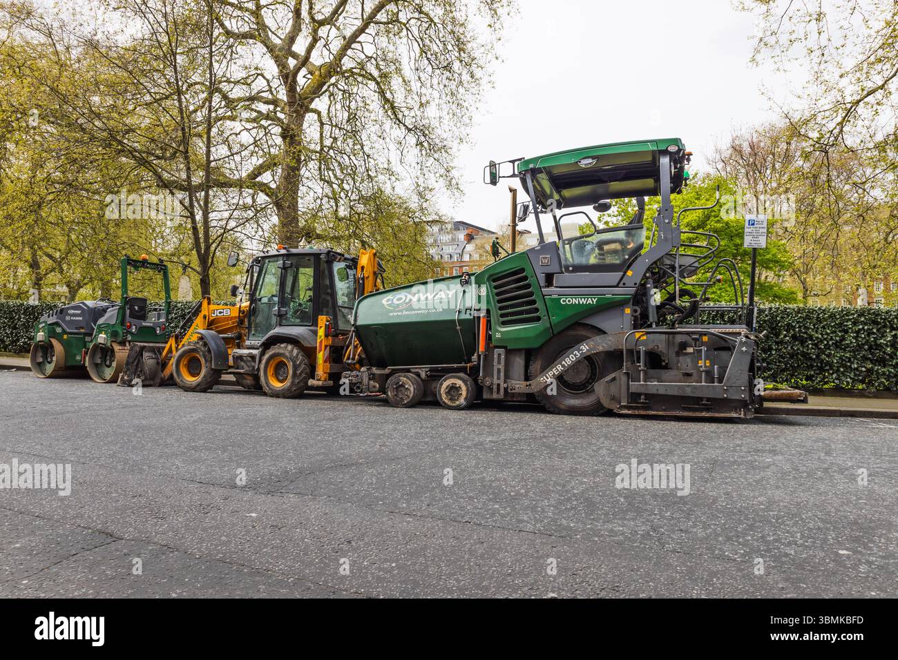 Linea di asfaltatrice, caricatore frontale e rullo parcheggiati su strada. Londra, Regno Unito, 14 aprile 2024 Foto Stock