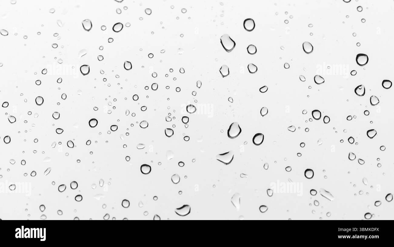 Le gocce di pioggia formano eleganti gocce su un vetro trasparente, creando un effetto sereno e naturale. Foto Stock
