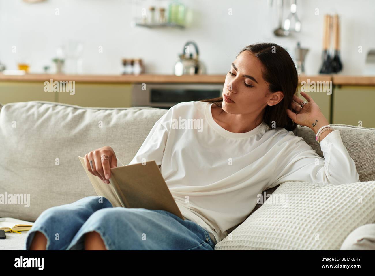 Rilassandosi a casa, la bella donna assorbe le pagine di un libro, circondati dal comfort. Foto Stock