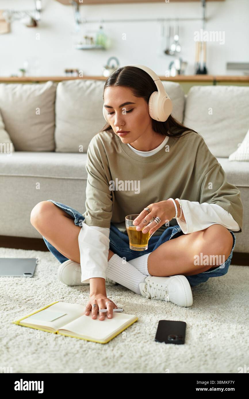 Rilassandosi a casa, una giovane donna scrive nel suo diario con musica che suona e beve in mano. Foto Stock