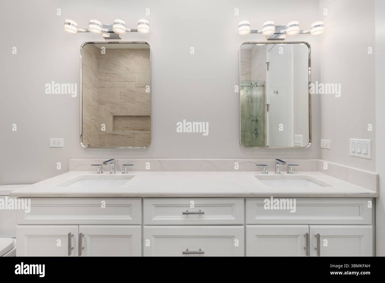 Bagno con armadio bianco, ripiano in marmo con rubinetti cromati e lampade moderne sopra gli specchi rettangolari. Foto Stock