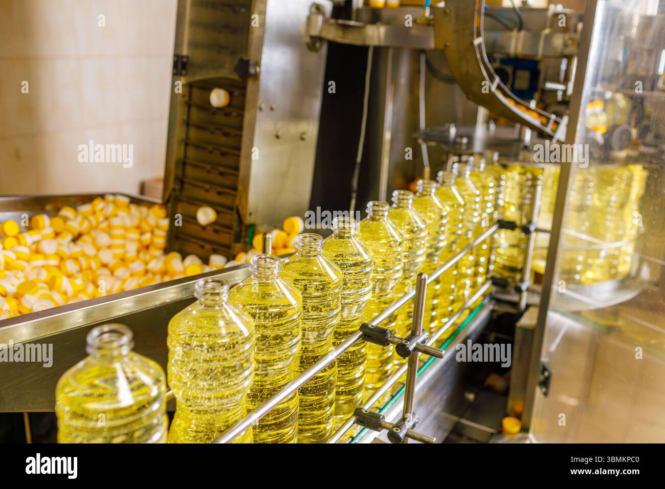 Linea di produzione automatizzata di olio di girasole in una fabbrica moderna con bottiglie trasparenti e macchinari di imbottigliamento avanzati Foto Stock