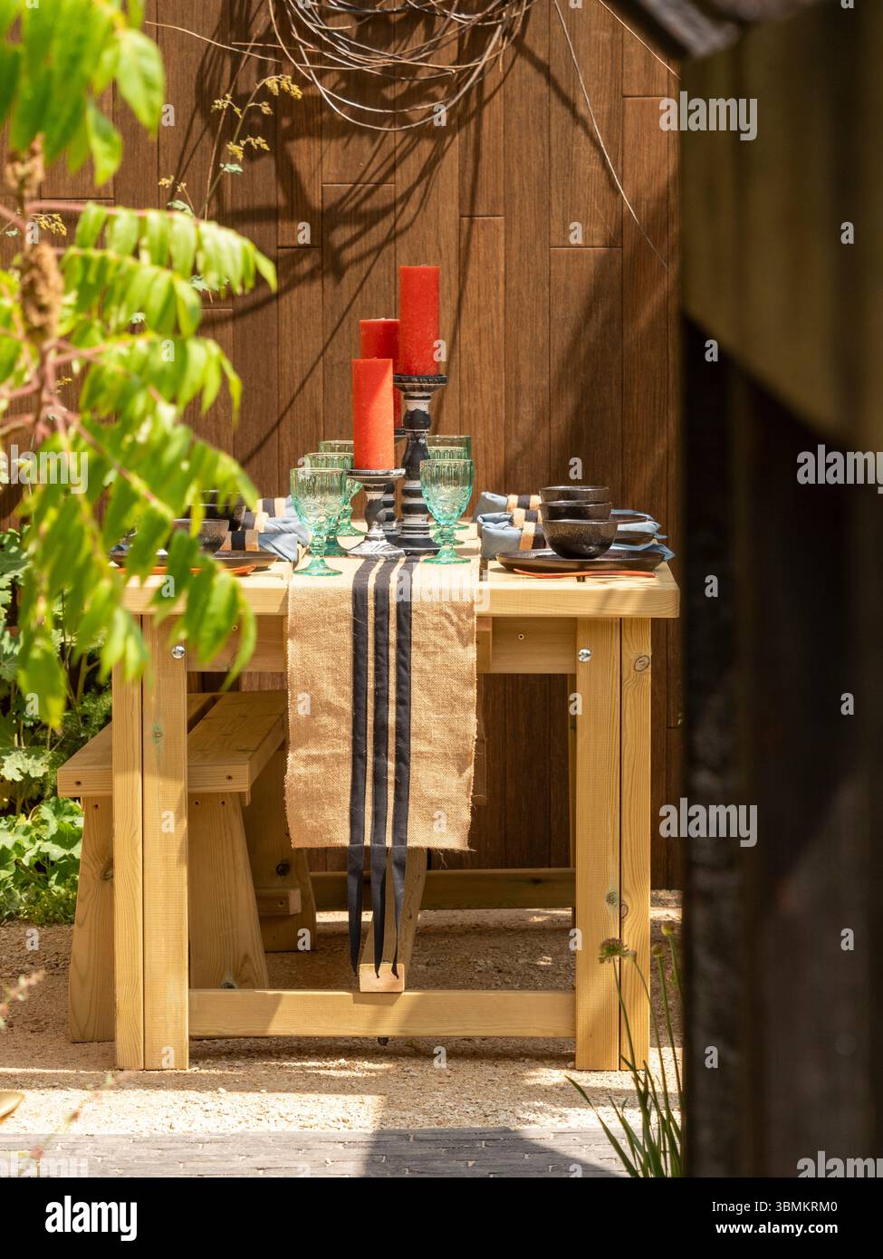 Tavolo da pranzo all'aperto con candele rosse, bicchieri e un corridore da tavolo in iuta a righe nel giardino a pianta di Nick Bailey al Gardeners World Live. REGNO UNITO Foto Stock