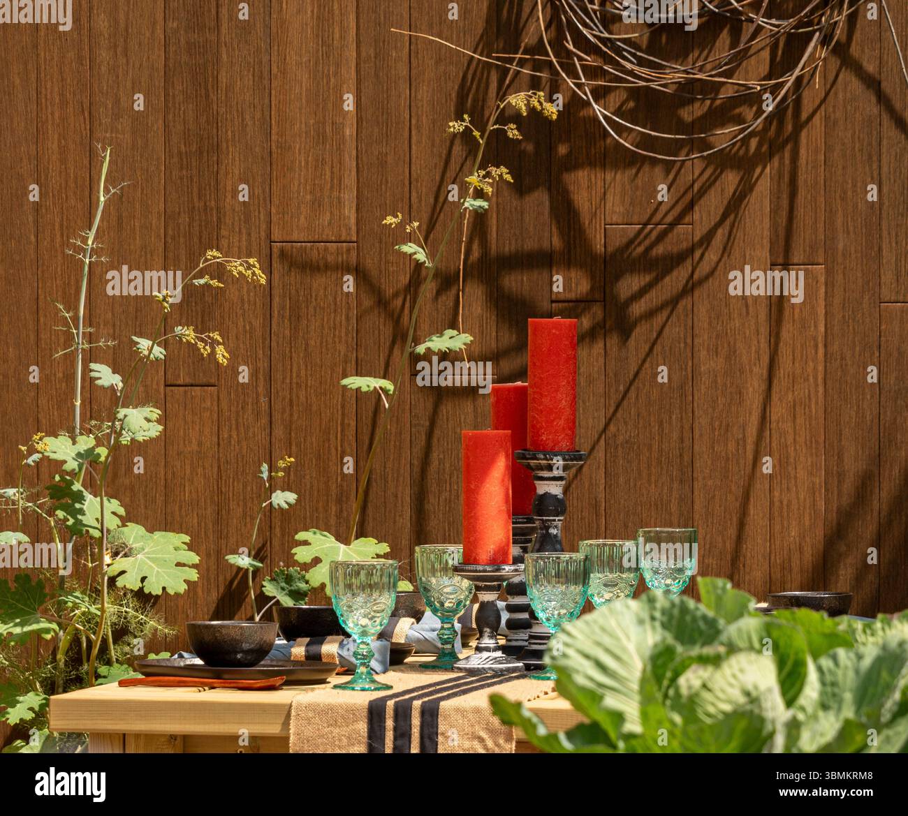 Tavolo da pranzo all'aperto con candele rosse, bicchieri e un corridore da tavolo in iuta a righe nel giardino a pianta di Nick Bailey al Gardeners World Live. REGNO UNITO Foto Stock