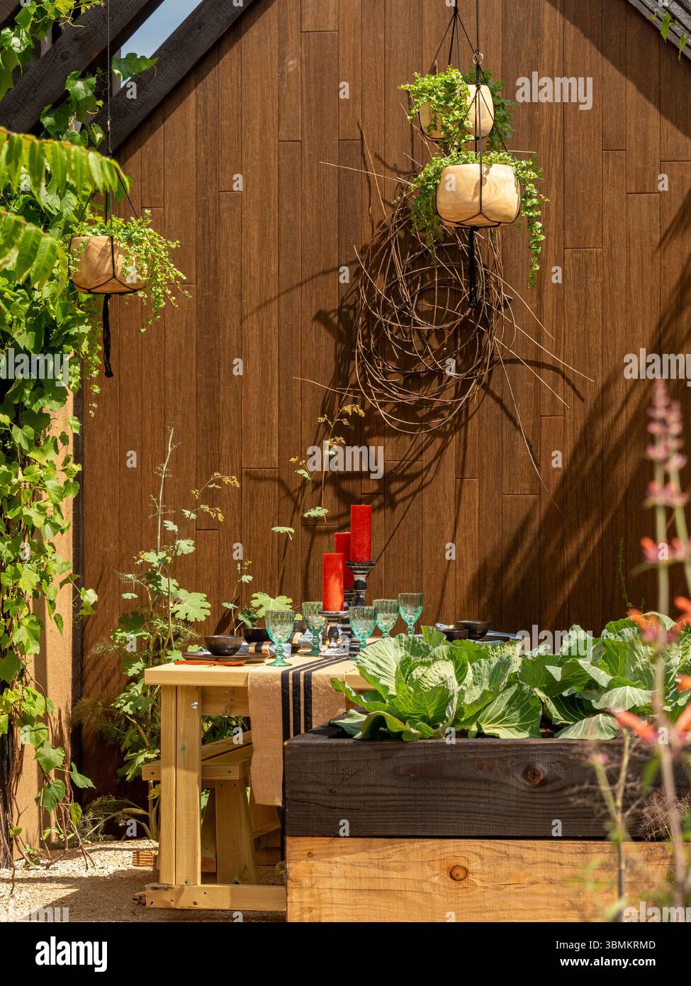 Tavolo da pranzo all'aperto con candele rosse, bicchieri e un corridore da tavolo in iuta a righe nel giardino a pianta di Nick Bailey al Gardeners World Live. REGNO UNITO Foto Stock
