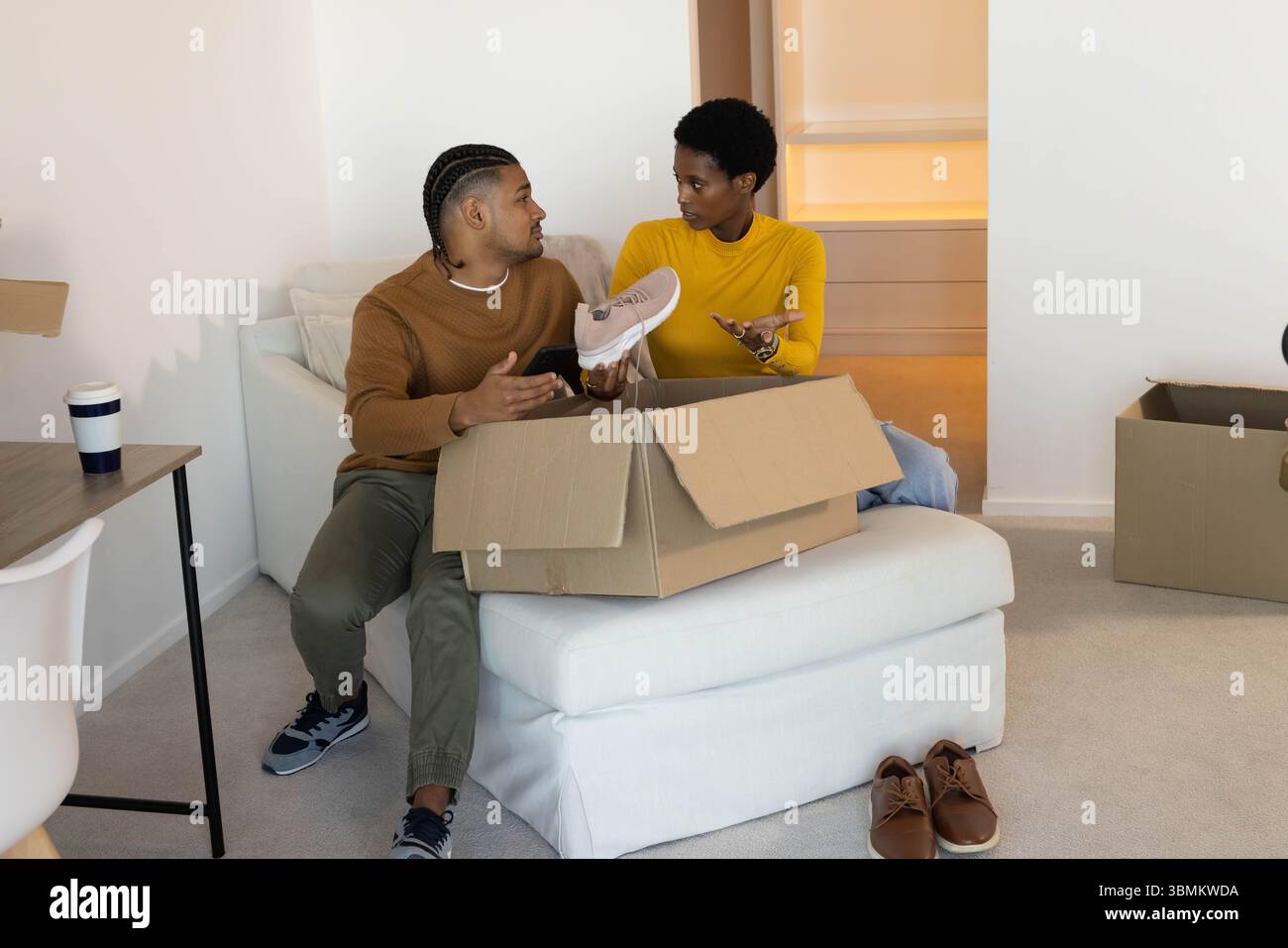 Sneakers unboxing diverse coppie sedute su ottomana nel soggiorno, con scatole mobili in cartone Foto Stock