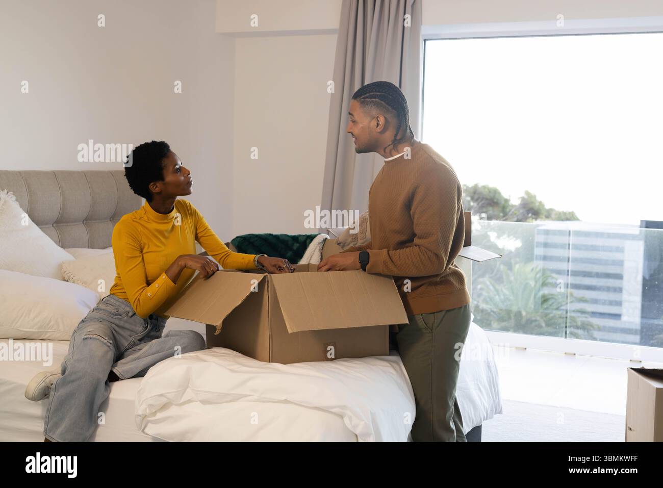 Diverse coppie che disimballano e smistano gli articoli sul letto in camera da letto, con scatola di cartone e smartphone Foto Stock