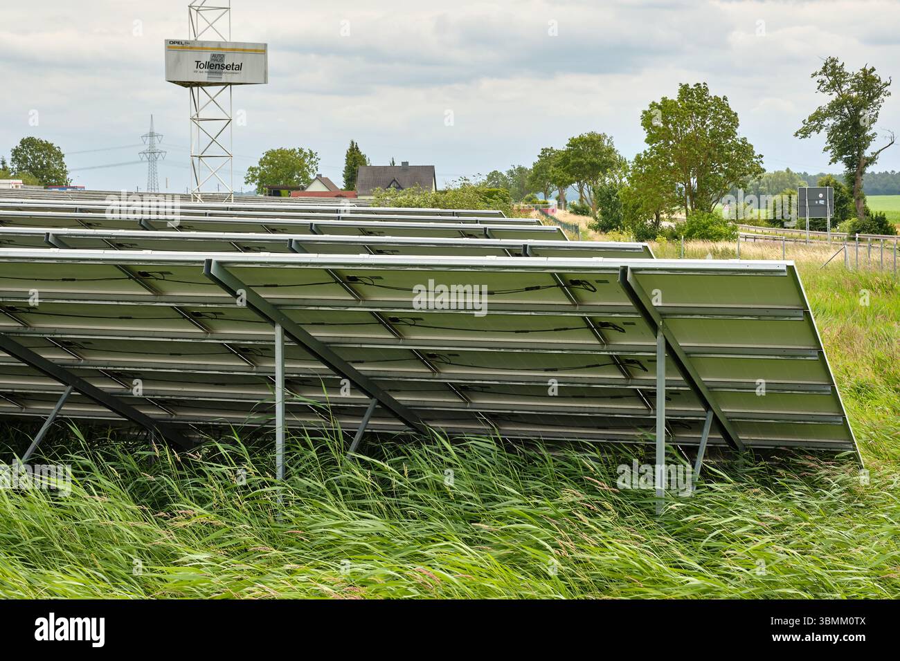 25 giugno 2024 - Altentreptow-Germania: File di pannelli solari su un campo verde vicino a un sito industriale sotto un cielo nuvoloso nel Meclemburgo, evidenziando re Foto Stock