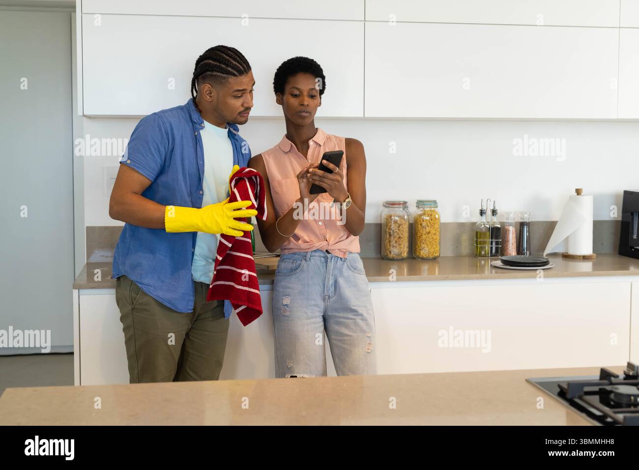 Pulizia coppia afroamericana appoggiata sul piano di lavoro in cucina, con guanto per pulizia Foto Stock
