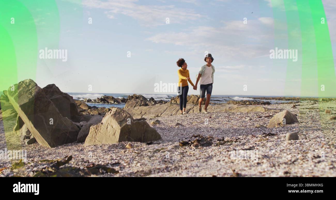 Uomo e donna che camminano tenendo le mani sulla costa rocciosa, con conchiglie di ciottoli e onde oceaniche Foto Stock