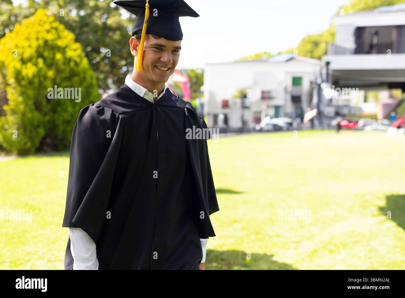 Laureato maschio bianco che indossa un abito nero con cappellino di Malta che cammina sul prato del campus, spazio fotocopie Foto Stock
