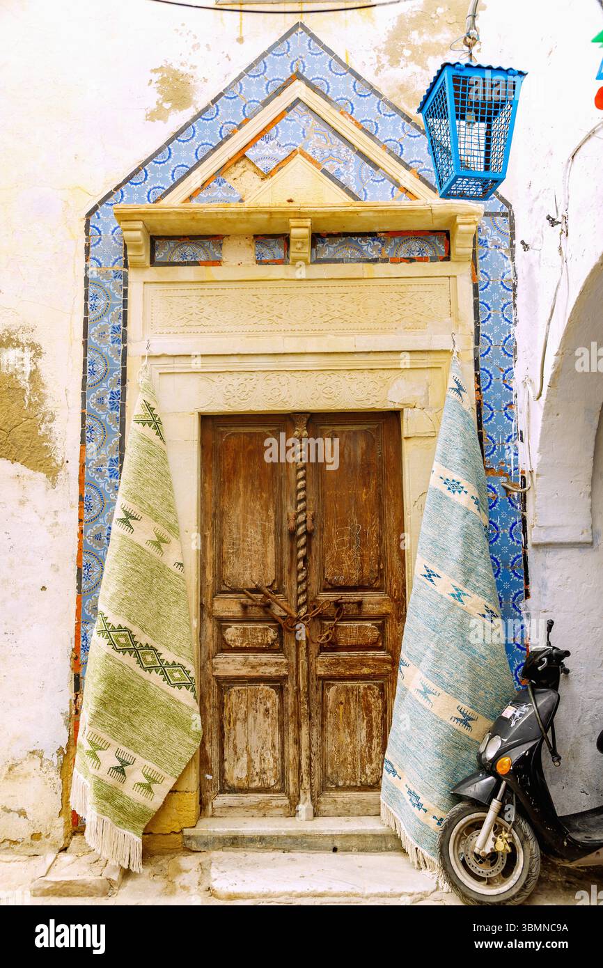 Casa tradizionale con porta storica in legno ornata con fregio a mosaico arabo e tappeti tessuti sulle pareti della casa in vendita ad Hammamet, Tunisia Foto Stock