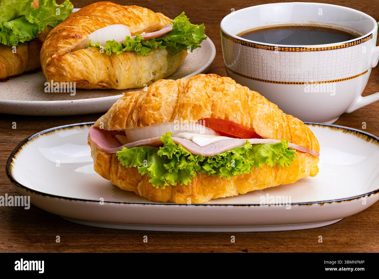 Croissant prosciutto in vassoio di ceramica bianco con bordo scuro e una tazza di caffè nero su un tavolo di legno. Foto Stock