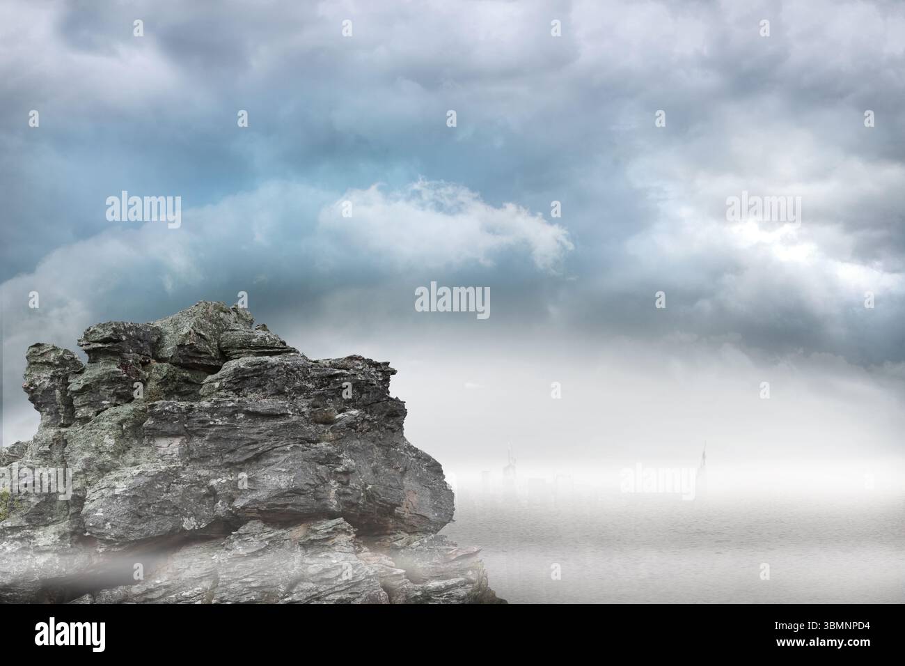 Design piatto che mostra la formazione rocciosa a sinistra, acqua calma, nebbia che avvolge lo skyline lontano, cielo nuvoloso Foto Stock