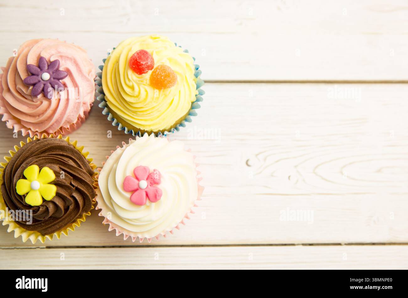 Mostra quattro cupcake sul tavolo, con glassa pastello, fiori fondenti, gomme Foto Stock